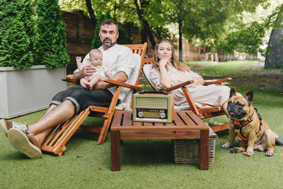 Family with baby and dog spending happy time together near trailer outside on deck chair, traveling