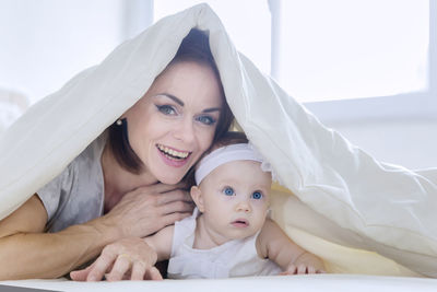 Portrait of smiling woman relaxing with baby girl on bed at home