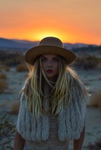 Close-up of young woman wearing warm clothing while standing against sun during sunset