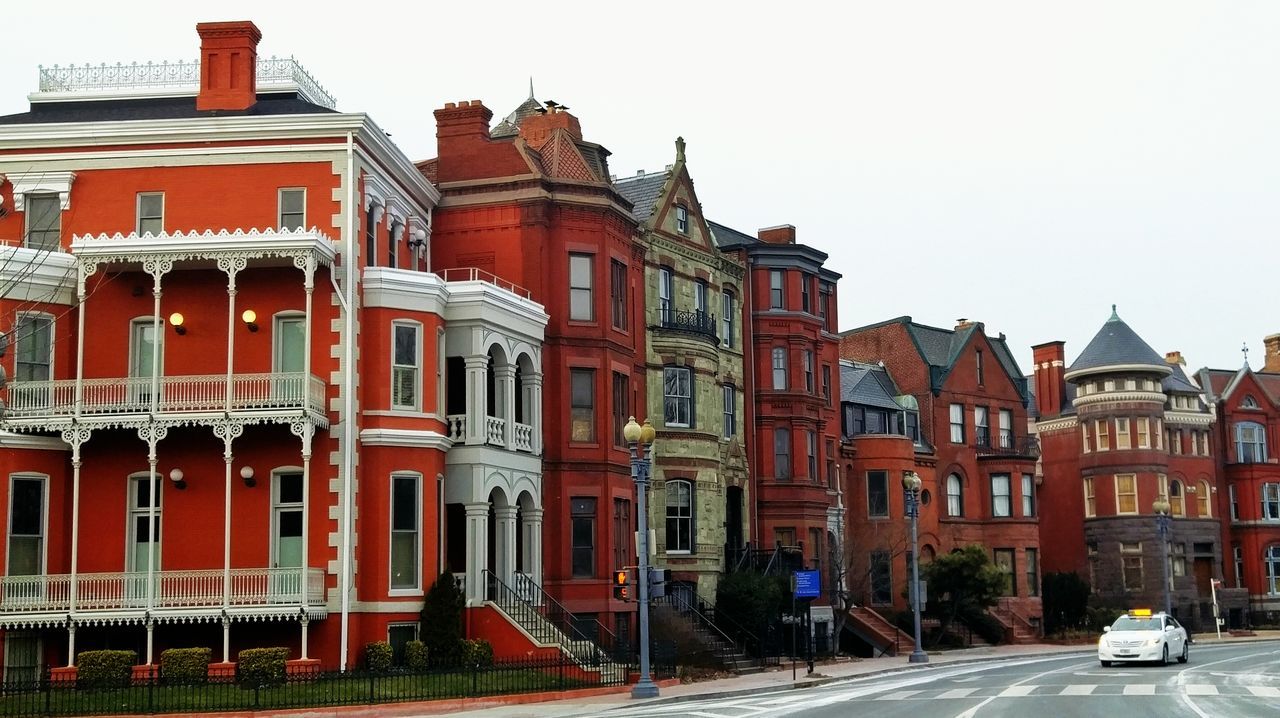 architecture, building exterior, built structure, transportation, street, clear sky, car, city, road, land vehicle, building, residential building, residential structure, mode of transport, window, outdoors, facade, street light, city life, incidental people