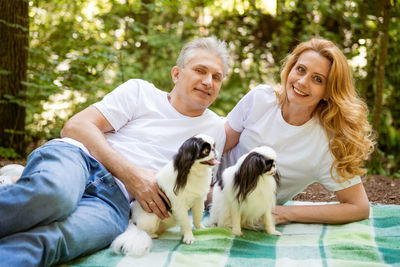 Mature couple in the forest lie on a blanket with a dog