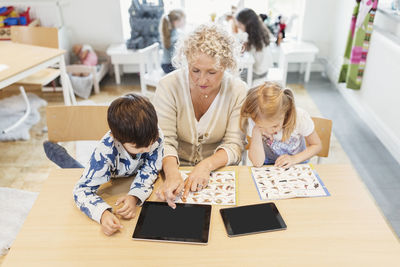 High angle view of senior teacher and children with animal charts and digital tablets