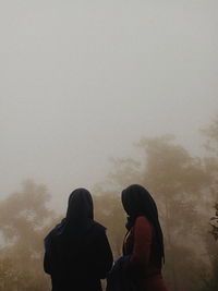 Rear view of people standing against sky during winter