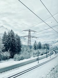 Snow covered trees by electricity pylon against sky