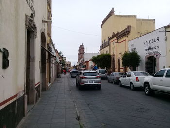 Cars on city street by buildings against sky