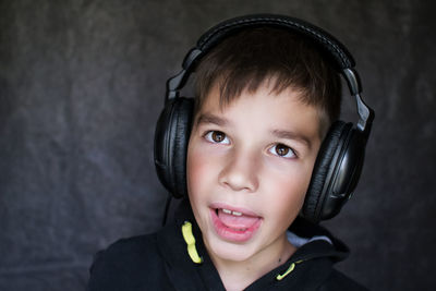 Close-up of boy listening music in headphones against wall