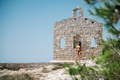 Woman wearing bikini standing against stone wall