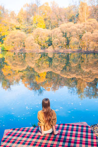 Rear view of woman sitting by lake during autumn