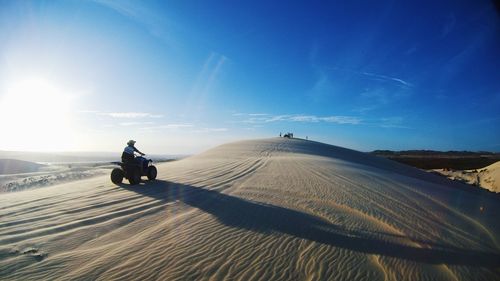 Man cycling on dirt road in desert against sky