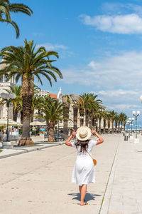 Rear view of woman wearing white sundress, walking on waterfront promenade in trogir, croatia