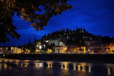 Illuminated buildings by river against sky at night