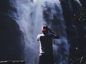 Rear view of man standing against waterfall