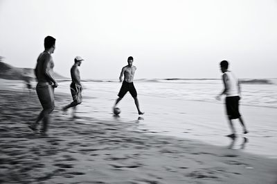 Male friends playing soccer on sea shore against clear sky