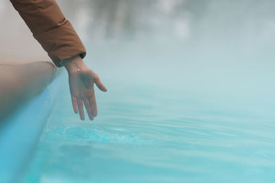 Hand of woman checking temperature of water in open swimming pool in winter. thermal spa outdoors.