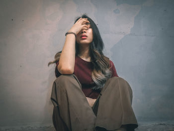 Young woman sitting against wall