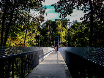 Distant view of woman walking on footbridge amidst trees at forest