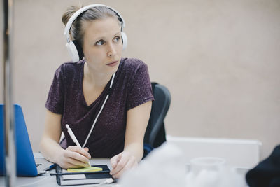 Female computer programmer looking away while writing on adhesive note in office