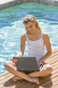 Young woman using laptop while sitting at poolside