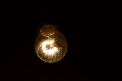 Low angle view of illuminated light bulb over black background