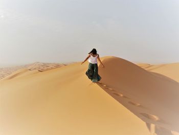 Rear view of young woman walking on sand dune at desert