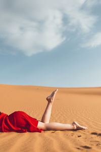 Woman lying on sand dune in desert against sky