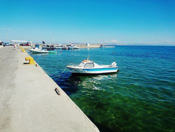 Boats moored at harbor against clear blue sky