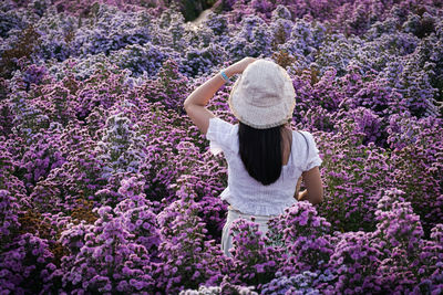 Rear view of woman standing amidst flowering plants