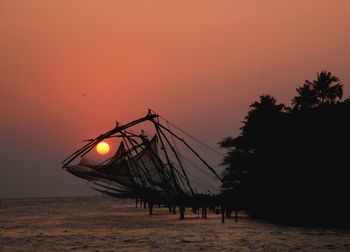 Silhouette fishing nets over sea against sky during sunset