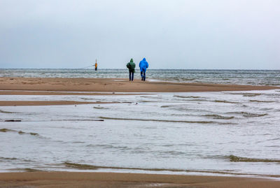 Rear view of people walking at beach against sky