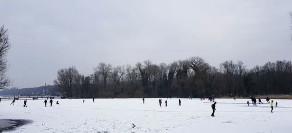 People on snowy field against sky during winter