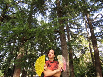 Smiling young woman standing amidst trees in forest