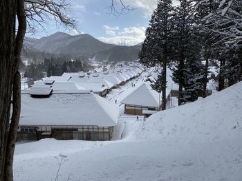 Snow covered houses by buildings against sky during winter