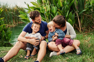 Full length of happy family sitting by pond