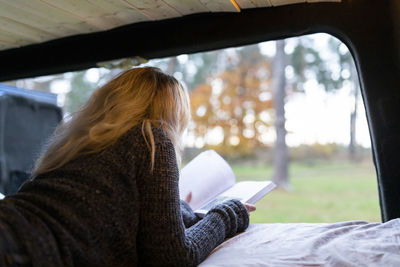 Midsection of woman using mobile phone while sitting on window