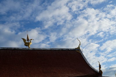 Low angle view of statue on roof of building against sky