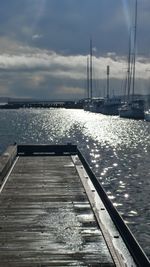 Sailboats on pier by sea against sky