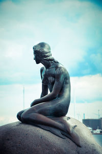 Statue of man sitting by sea against sky