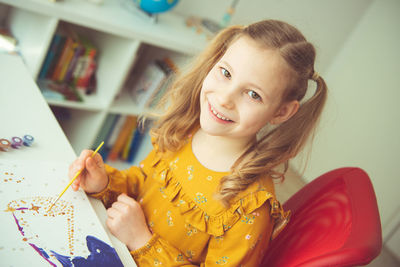 Portrait of cute girl painting while sitting at home