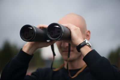 Close-up of mid adult man looking through binoculars while standing against sky
