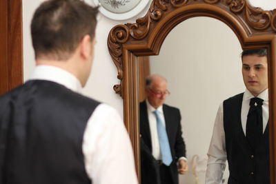 Rear view of groom reflecting in mirror at home