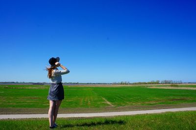 Rear view full length of young woman standing on field against clear blue sky