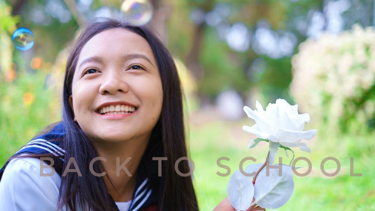 PORTRAIT OF SMILING YOUNG WOMAN WITH FLOWERS IN MOUTH