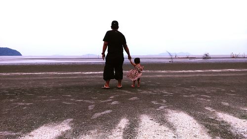 Rear view of father and daughter standing on landscape against clear sky