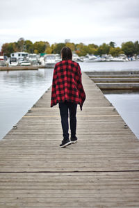 Rear view of woman standing on pier over lake against sky