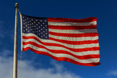 Low angle view of american flag waving against blue sky