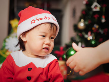 Close-up of mother giving christmas decoration to baby boy at home