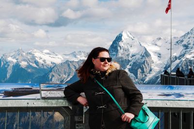 Woman in sunglasses standing against snowcapped mountains