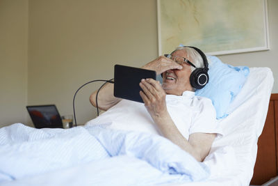 Senior man rubbing eyes while using digital tablet on bed in hospital ward