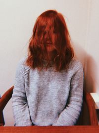 Rear view of woman sitting on chair against wall