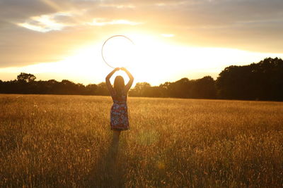 Woman standing on field against sky during sunset